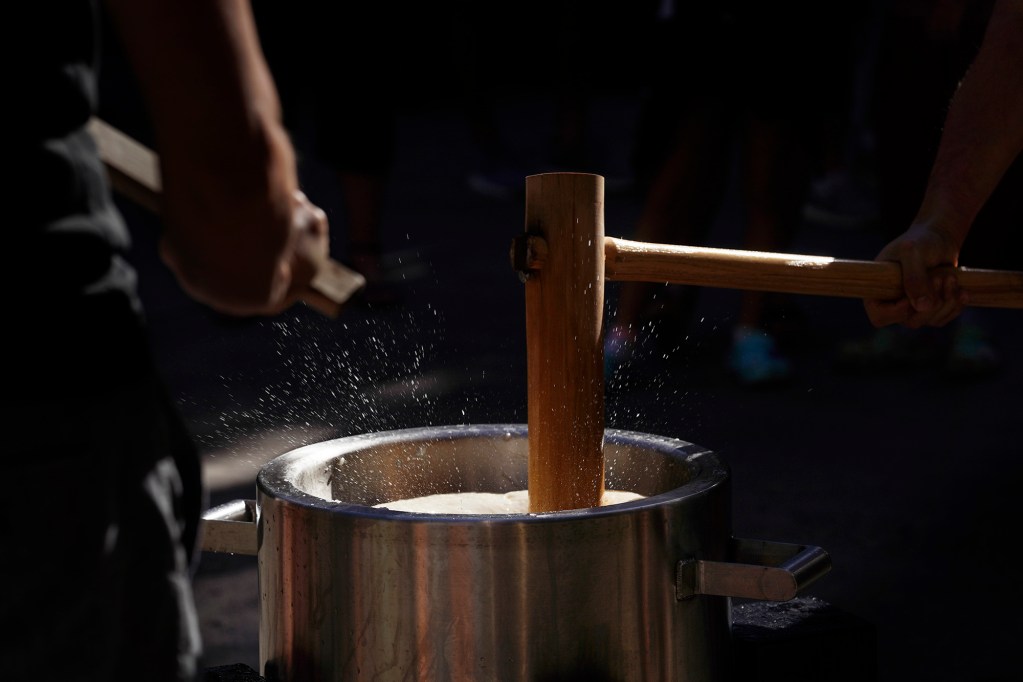 A kine (wooden mallet) makes water spray off the mochi in the usu (mortar) during the Konko Mission of Wahiawa’s traditional new year’s mochitsuki (mochi pounding) demonstration for Prince Waikiki Hotel guests Wednesday, Dec. 27, 2023, in Honolulu. This usu is a custom made, stainless steel mortar created by head minister Yasuhiro Yano. The making of mochi (chewy rice cake) and consuming it is a Japanese new year tradition. Eating mochi is said to bring good luck. (Kevin Fujii/Civil Beat/2023)