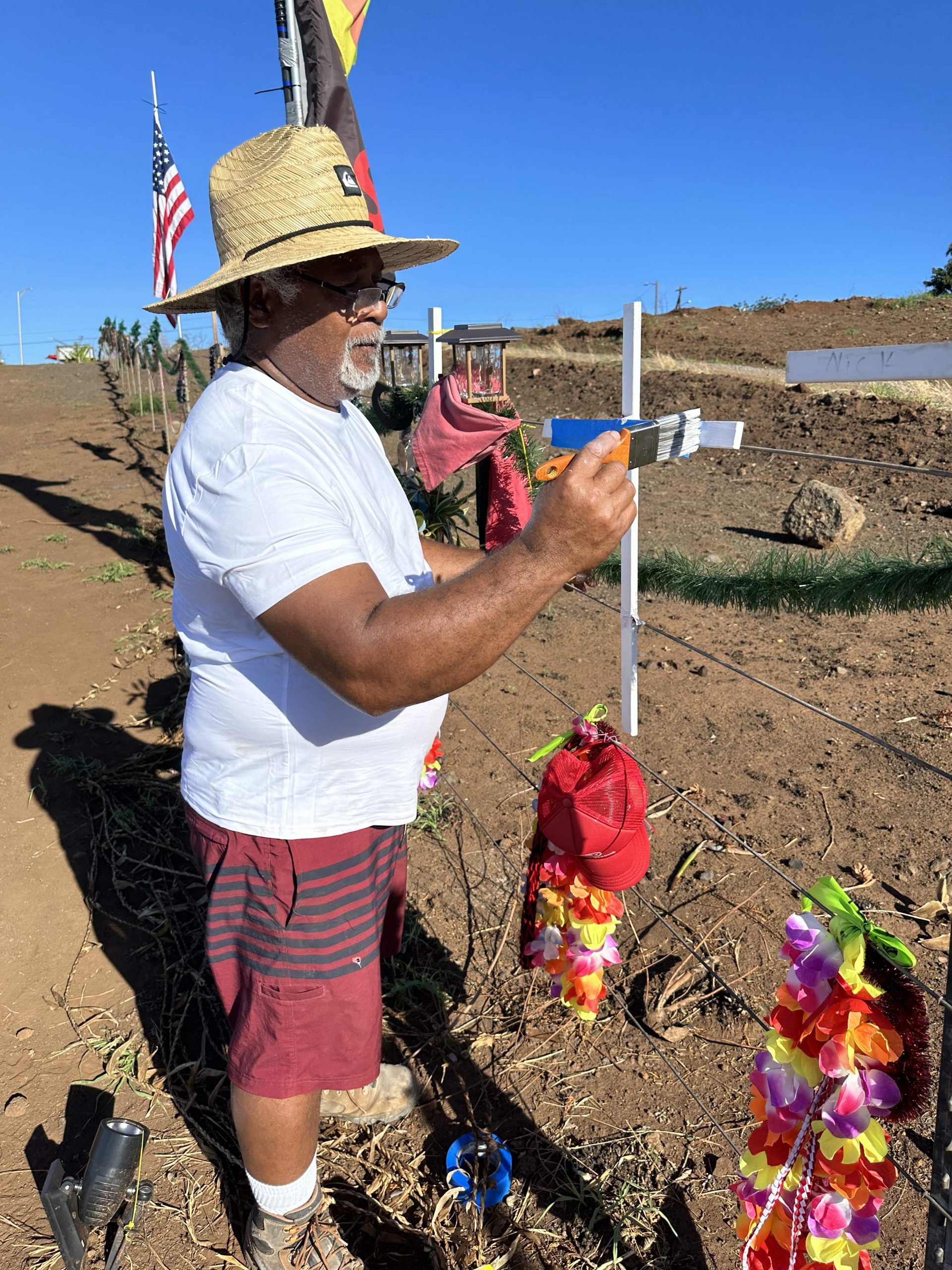 Soakai Taufa applied fresh paint to a cross on the roadside memorial to Lahaina wildfire victims on Saturday, 12/9/2023. Taufa, a carpenter, supplied the crosses for the grassroots effort. (Christie Wilson/Civil Beat/2023)