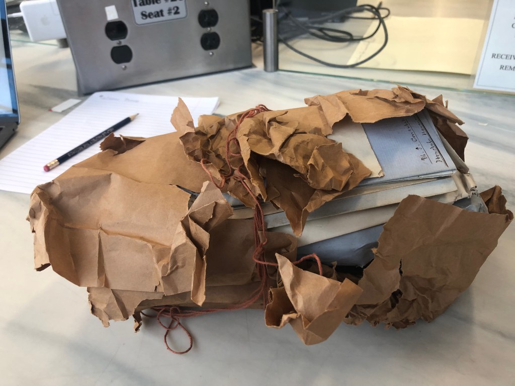 A thickly bundled brown paper packet tied together with red strings and containing letters and other items.