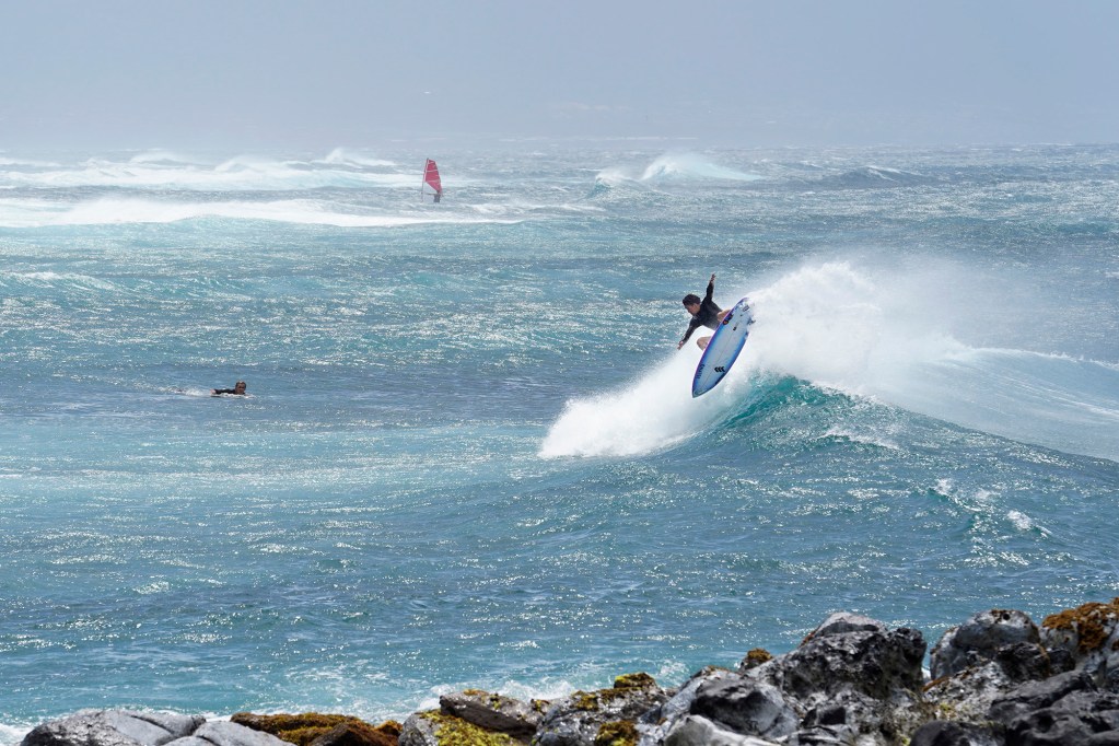 Despite a strong side wind and rain obscuring Central Maui, professional surfer Jackson Bunch of Paia does and air at Pavilions off Ho’okipa Beach Park Tuesday, April 2, 2024, in Maui. Life is returning to normal for some on the Valley Isle. (Kevin Fujii/Civil Beat/2024)