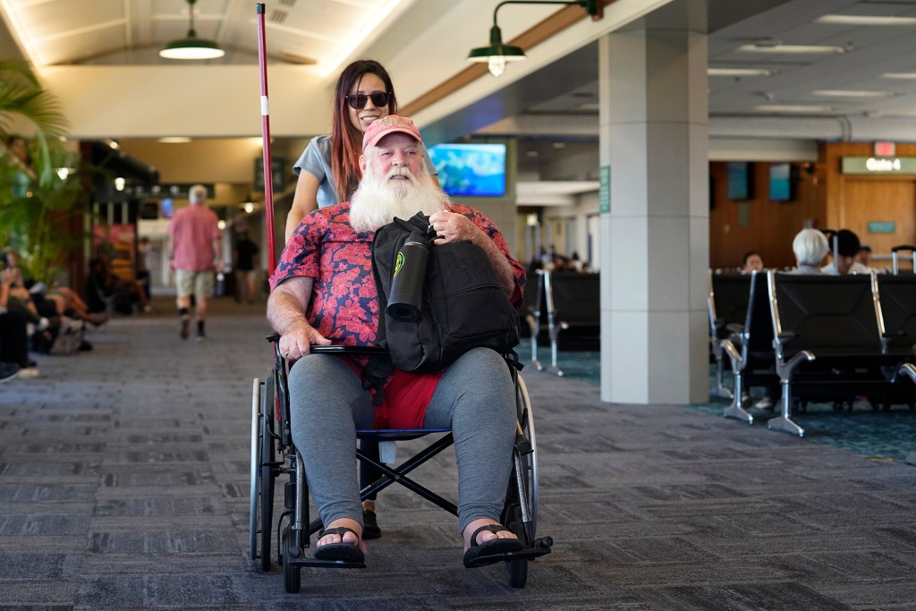 Prime Flight Aviation Porter Margarita Perez gives Ron Proctor his last sleigh ride through the airport Tuesday, April 9, 2024, in Kahului. Proctor lived in Lahaina for 12 years. The Aug. 8 fire set things in motion for him to return to Napa, Calif., despite trying to stay in Maui. (Kevin Fujii/Civil Beat/2024)