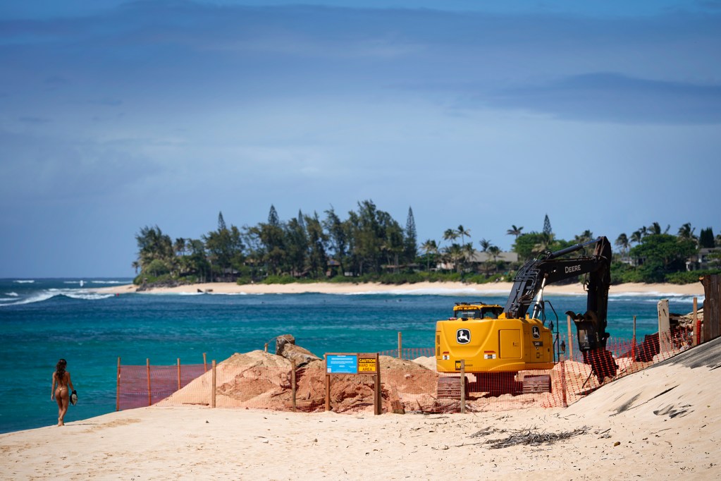 A beach goer walks around a fence for seawall removal at a Sunset Beach house Tuesday, May 7, 2024, in Pupukea. (Kevin Fujii/Civil Beat/2024)