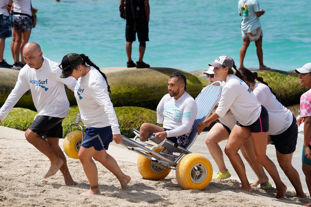 Transition volunteers escort Jose Martinez of the USA after his first heat in the 2024 Hawaii Adaptive Surfing Championships Prone Assist division Monday, May 13, 2024, in Honolulu. (Kevin Fujii/Civil Beat/2024)