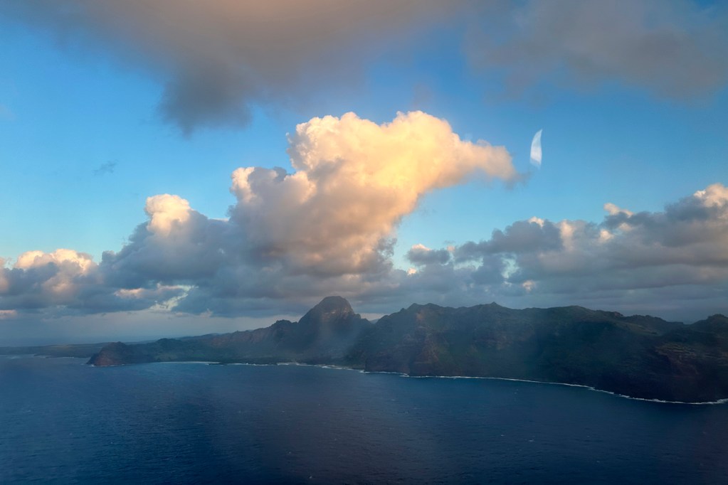 The rugged southern coast of Kauai is photographed from a commercial airplane landing at Lihue Airport Monday, June 10, 2024. Ghost-like aberrations are hard-water spots on the exterior of the glass and some reflections from inside the plane are visible too. (Kevin Fujii/Civil Beat/2024)