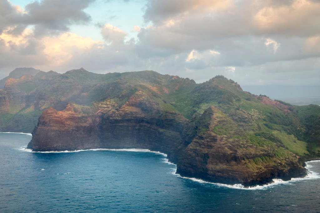 The rugged southern coast of Kauai is photographed from a commercial airplane landing at Lihue Airport Monday, June 10, 2024. Ghost-like aberrations are hard-water spots on the exterior of the glass. (Kevin Fujii/Civil Beat/2024)