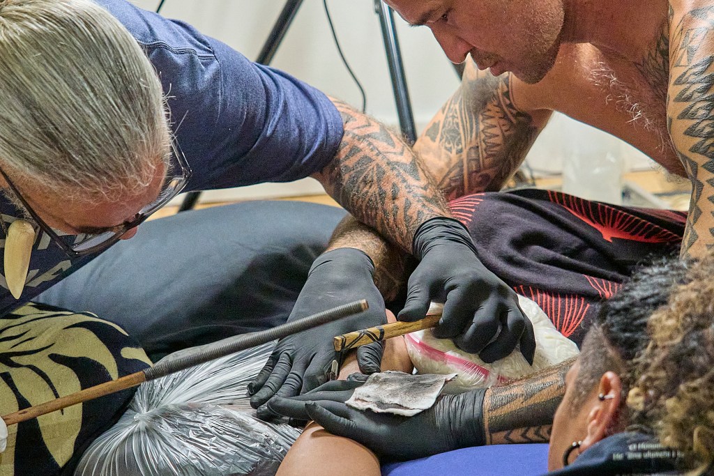 FestPac continued on June 11th at Capital Modern with exhibitions, displays and dance performances. Tattoo Artist Kawika Au (L) with assistance from his student Chris Love (R), creates a wrist tattoo for a client at the Capital Modern exhibitions during the Festpac celebrations (David Croxford/Civil Beat/2024)