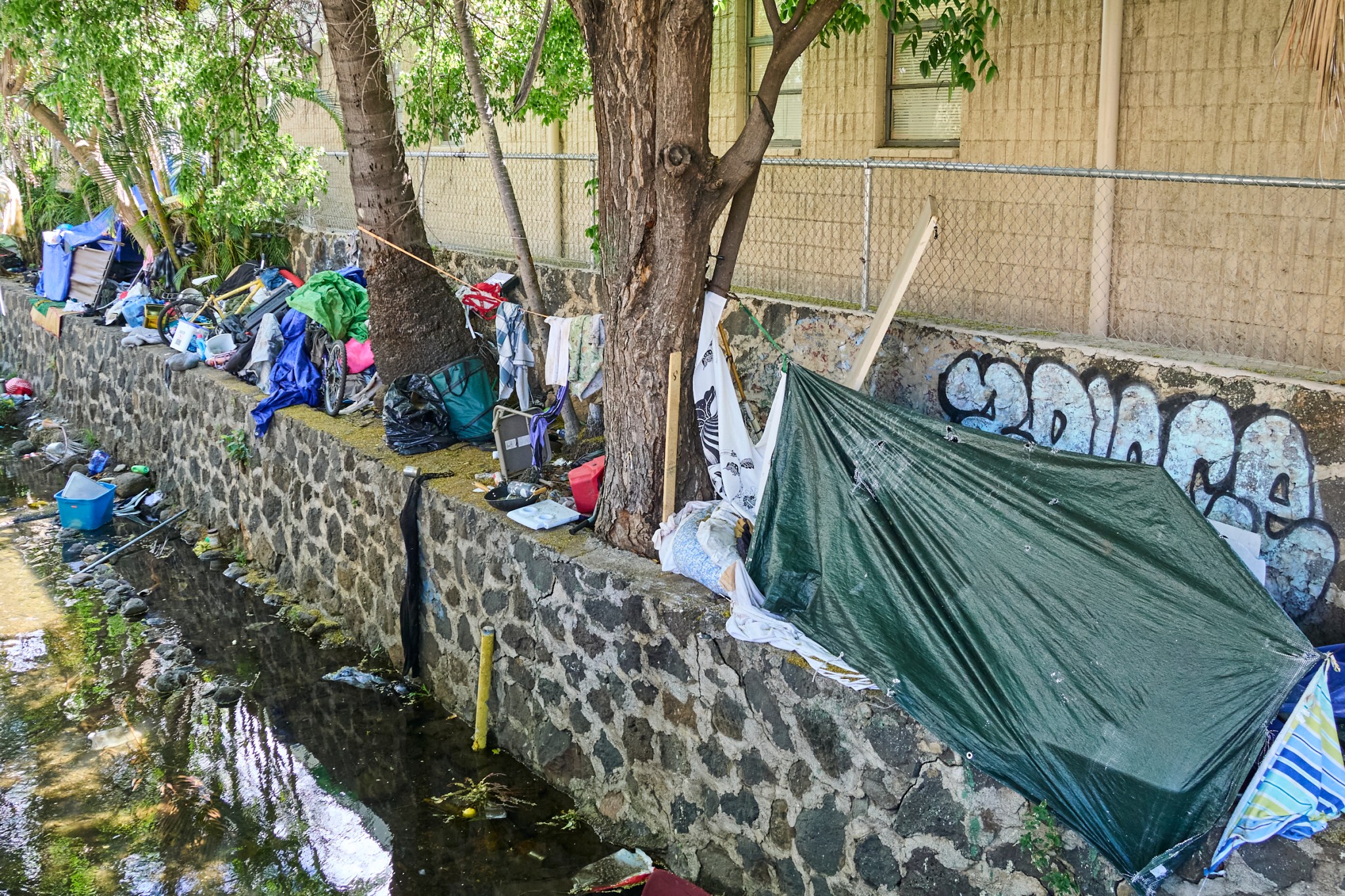 Along the Diamond Head side of Kalakaua Avenue there is a growing homeless encampment dotted along the stream that parallels the famously named street. Some of the tents surround a Bus stop within eyesight of the local Jack in the Box. The assortment of trash ranges from Shopping Carts to displaced Yeti water flasks and everything in between. Photographed Wednesday June 12, 2024(David Croxford/Civil Beat/2024)