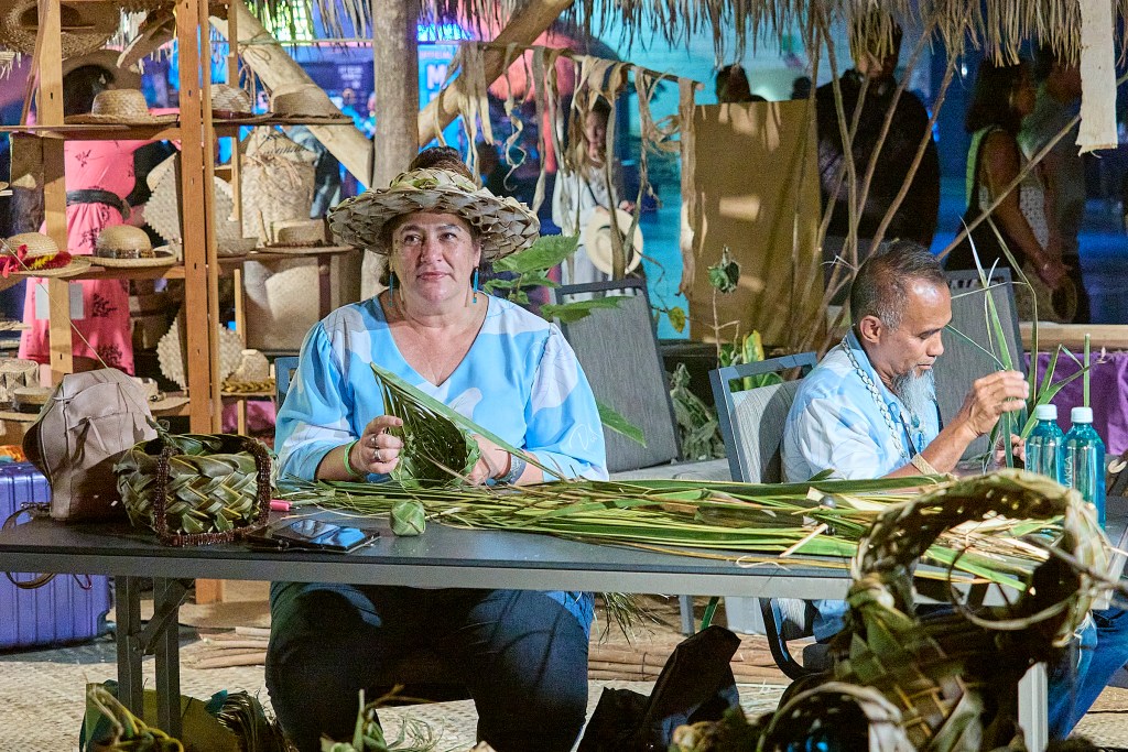 U'i Kahue-Cabanting and Mario Siatris weave coconut fronds at FestPac.  Photographed June 13th, 2024 in the Hawaii Hale.(David Croxford/Civil Beat/2024)