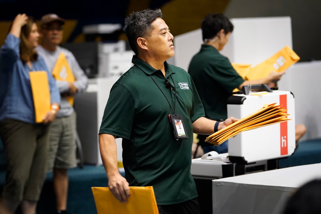 Chief Elections Officer Scott Nago hands out test ballots to test the vote counting system for the primary election Saturday, July 27, 2024, in the Hawaii State Capitol Senate Chambers in Honolulu. Official observers conducted the test. They serve as the public’s, “eyes and ears,” from different political parties, community groups and individuals interested in the voting process. (Kevin Fujii/Civil Beat/2024)