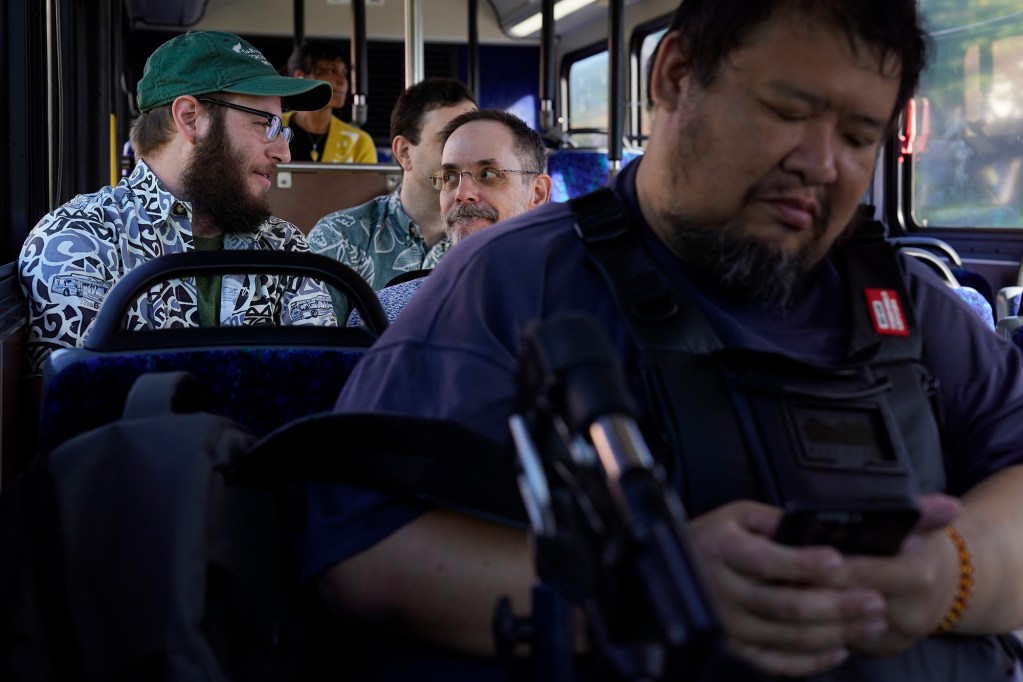 Reed Mershon, left, chats with Aaron Pietruszka, center, while Brendan Mar checks his phone on one of The Bus route 18’s last rounds Thursday, Aug. 15, 2024, in Honolulu. The three riders and Yosef Ben Gershom, seated behind Pietruszka, all met on Route 18. The route will be discontinued. Some regular riders have found a community with each other and the driver. (Kevin Fujii/Civil Beat/2024)