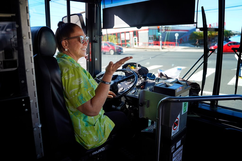 The Bus route 18 driver Kathy Paiva blows a kiss to a long-time passenger on the route’s final lap Thursday, Aug. 15, 2024, in Honolulu. Paiva has been driving for 28 years. The route will be discontinued. Some regular riders have found a community with each other and the driver. (Kevin Fujii/Civil Beat/2024)