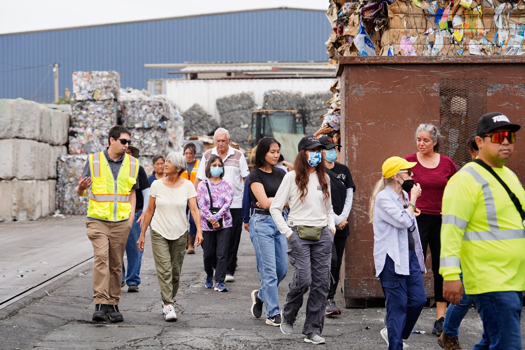 Tour de Trash participants walk among the bailed corrugated cardboard and aluminum cans Wednesday, Aug. 28, 2024, in Kapoeli. The City and County of Honolulu sponsors the tour to follow the journey of Oahu residents and visitors’ rubbish, recyclable items and compostable/green waste take through the collection and disposal process. (Kevin Fujii/Civil Beat/2024)