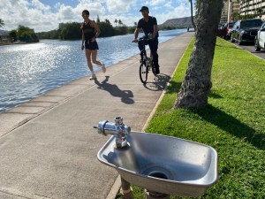 Runners pass near a water fountain that is missing its handle and water spout on the pathway along the Ala Wai Canal. (Denby Fawcett/Civil Beat/2024)
