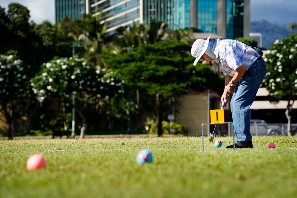 Gateball player Steven Kaneshiro strikes a ball toward the first gate during practice Wednesday, Sept. 4, 2024, at Ala Moana Beach Park in Honolulu. Kaneshiro discovered the sport after re-connecting with Art Kimura. Kimura was one of Kaneshiro’s high-school teachers. (Kevin Fujii/Civil Beat/2024)