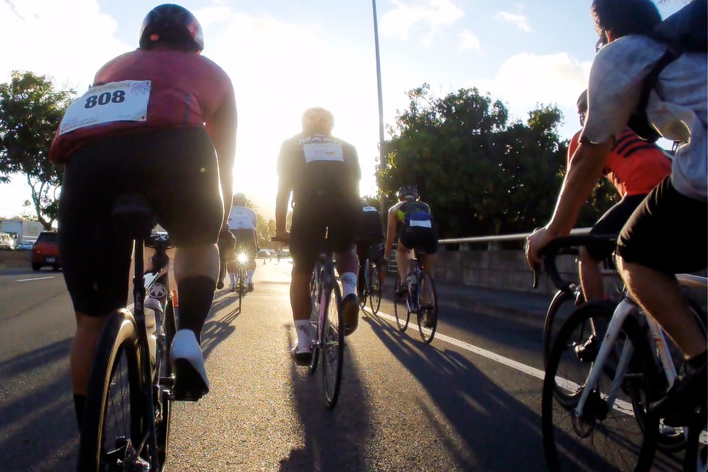 Cyclists ride into the sunrise near the beginning of the Honolulu Century Ride Sunday, Sept. 29, 2024, in Honolulu. This is the Hawaii Bicycling League’s biggest fundraiser and the state’s largest cycling event with more than 1,300 registered riders. Bicyclists could choose to ride 25, 50, 75 or 100 miles. The Aloha Fun Ride also took place for younger riders and families simultaneously. Still photo taken from video. (Kevin Fujii/Civil Beat/2024)