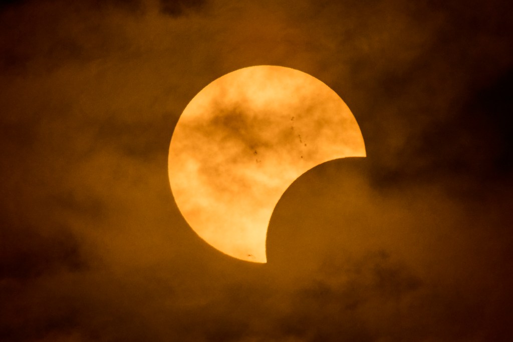 The partially eclipsed sun peaks in between the cloud bank the settled to eliminate a completely clear view of the phenomena. Photographed on October 2, 2024. A closer peak at our closest star yields that it was experiencing some sunspots behind the clouds.(David Croxford/Civil Beat/2024)(David Croxford/Civil Beat/2024)