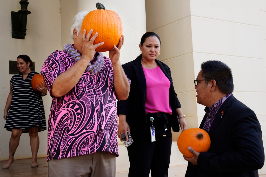 Kauai County Council Vice Chair KipuKai Kuali’i hides behind a pumpkin before a group photo with the 11th Annual Harvest Festival organizers Wednesday, Oct. 9, 2024, in Lihue. Council member Addison Bulosan, right, looks on. (Kevin Fujii/Civil Beat/2024)