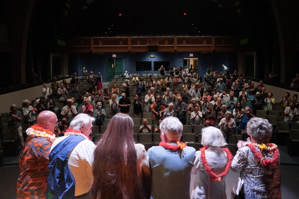Storytellers gather on stage as the audience applauds the featured Kupuna
