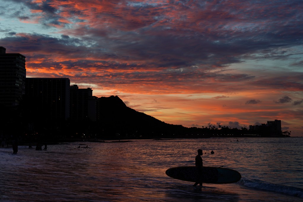 A stand-up paddleboarder enters the water as the sun rises over Honolulu’s famous Waikiki Beach Wednesday, Oct. 23, 2024. (Kevin Fujii/Civil Beat/2024)