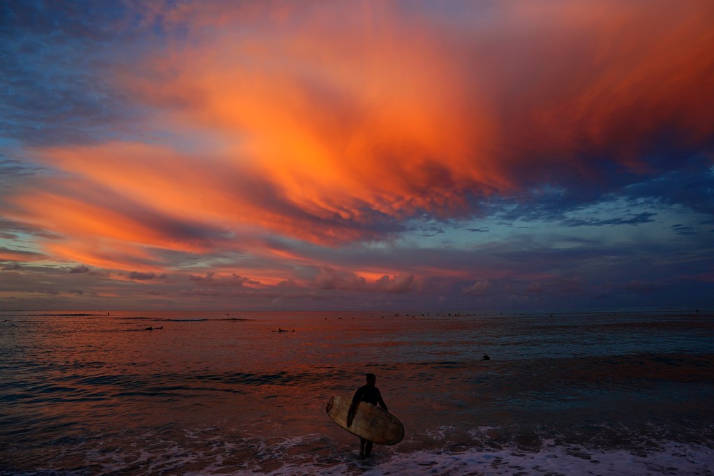 Five Ton Jack (the name the surfer gave) wraps up a dawn-patrol session as the sun paints the clouds over Canoes surf break off Honolulu’s famous Waikiki Beach Wednesday, Oct. 23, 2024. (Kevin Fujii/Civil Beat/2024)