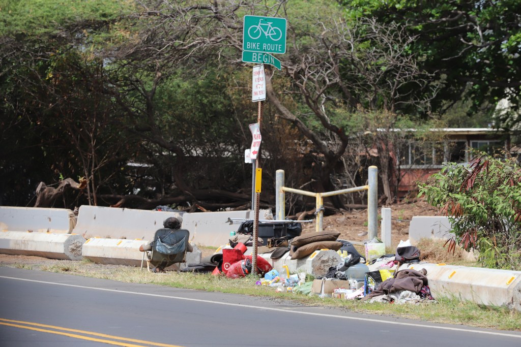 A man who appears to be homeless enjoys the sun, sitting on a beach chair near his belongings at Amala Place, across the street from Island Grocery Depot in Kahului. (Leo Azambuja/Civil Beat/2024)