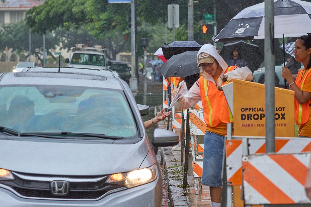 Voters in early voting at Honolulu Hale on King Street in Honolulu were met with torrential downpours as they drove through the election only lane that had been set aside and coned to allow drivers to either hand off their ballots to Poll workers or drop them into several Ballot boxes placed and manned along King Street. (David Croxford/Civil Beat/2024)
