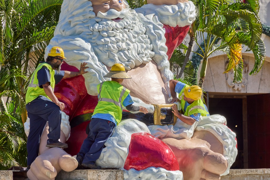 After Honolulu’s own Shaka Santa was secured in his annual seat outside Honolulu Hale, City crews worked to place his belt buckle in the correct location.  Coupled with Mrs Claus the Festive pair will be one of the main display elements for the Honolulu City Lights Parade on December 7th (David Croxford/Civil Beat/2024)