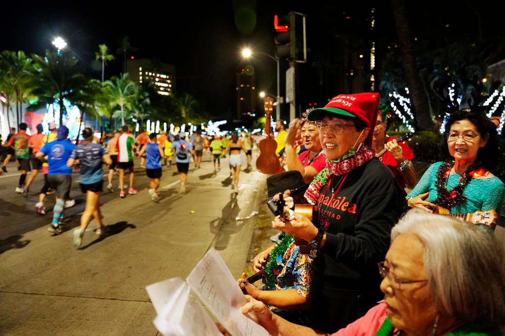 Papakōlea Anakala Anakē (PAA) serenade Honolulu Marathon runners with Christmas carols across from Honolulu Hale Sunday, Dec. 8, 2024, in Honolulu. PAA sang traditional and local Christmas songs including the “12 Days of Christmas (Hawaiian style),” which uses, “One mynah bird in one papaya tree,” refrain instead of, “A partridge in a pear tree.” (Kevin Fujii/Civil Beat/2024)
