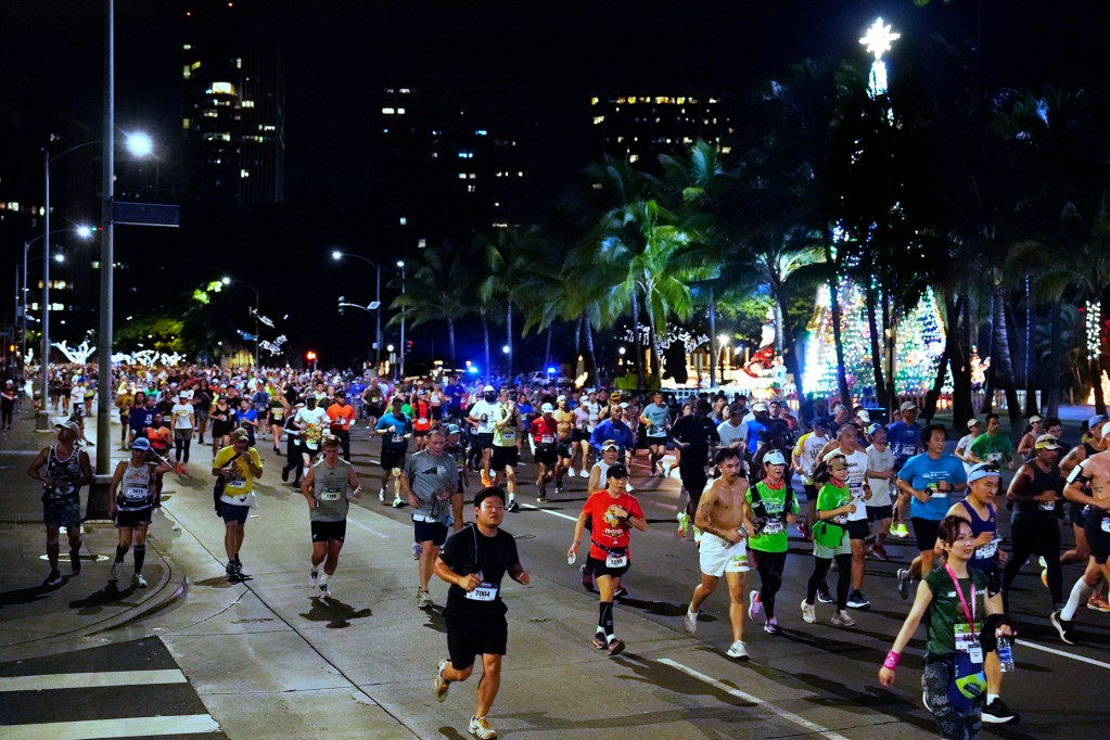 Honolulu Marathon runners past Christmas decorations at Honolulu Hale Sunday, Dec. 8, 2024, in Honolulu. This marks the 52nd Honolulu Marathon. More than 35,000 registered to run, walk, roll 26.2 miles, Start to Park 10K or the Kalakaua Merrie Mile. (Kevin Fujii/Civil Beat/2024)