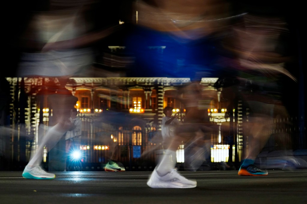 Runners pass Iolani Palace Sunday, Dec. 8, 2024, in Honolulu. This marks the 52nd Honolulu Marathon. More than 35,000 registered to run, walk, roll 26.2 miles, Start to Park 10K or the Kalakaua Merrie Mile. The shoes hit the pavement for a fraction of a second while the runners’ bodies are moving which causes the blur. Exposure for this photo is set at ISO 1600, aperture f4.5, shutter 1/8. (Kevin Fujii/Civil Beat/2024)