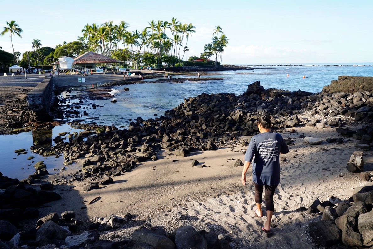 Cindi Punihaole with ReefTeach at Kahalu’u Bay Education Center, walks toward Kahalu’u Bay Wednesday, Dec. 11, 2024, in Kailua-Kona. A damaged fish pond is on the left. (Kevin Fujii/Civil Beat/2024)
