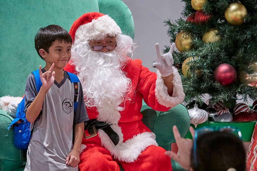 Hearing impaired children from around the state gathered on Thursday December 12th to be entertained and to meet up with a Santa Claus who could speak their language. Although some of the children were reluctant to practice their signing skills, most were able to communicate their Christmas gift Wishes to the man in the red suit. 9 yr old Ezra Corniel who has ear implants and an aid, shares the ASL gesture for ÒI love youÓ with Santa and his audience bound family.(David Croxford/Civil Beat/2024)