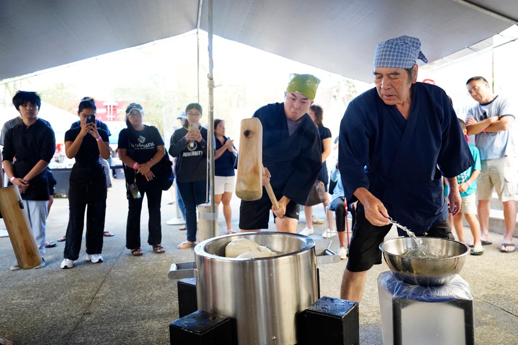 After four kine (wooden mallets) take turns pounding mochigome (glutinous rice) into a dough-like ball, Konko Mission of Wahiawa head Rev. Yasuhiro Yano, right, adds more water and turns the mochi while alternating hits with Nick Furusho during a mochitsuki demonstration Saturday, Dec. 14, 2024, at the Japanese Cultural Center of Hawai’i in Honolulu. A part of the mochitsuki tradition is having trust with whom you’re working. (Kevin Fujii/Civil Beat/2024)