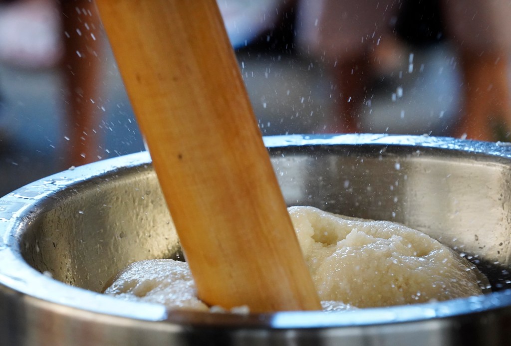 Water flies as a kine (wooden mallet) pounds the mochigome (glutinous rice) as water is added during a Konko Mission of Wahiawa mochitsuki demonstration Saturday, Dec. 14, 2024, at the Japanese Cultural Center of Hawai’i in Honolulu. What began as a regular looking, 10-pound bowl of rice will soon become a rice cake enjoyed for thousands of years in China and Japan. (Kevin Fujii/Civil Beat/2024)