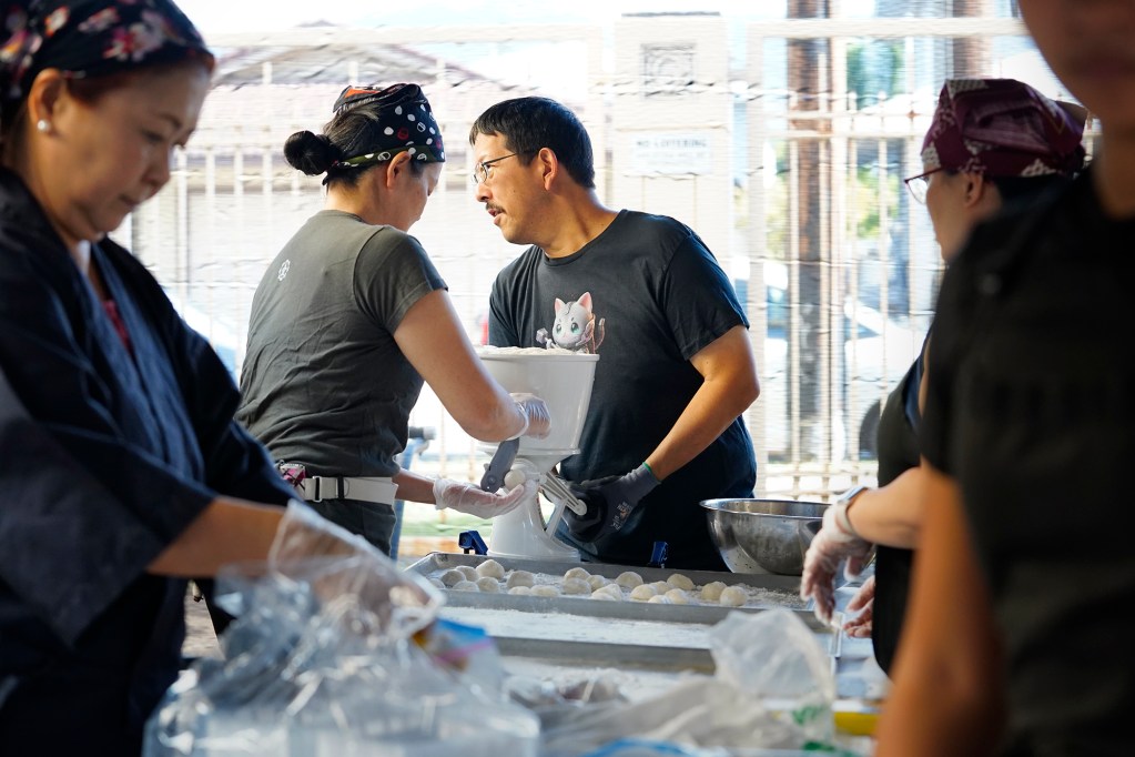 The Konko Mission of Wahiawa Rev. Edna Matsuoka, second left, cuts mochi while her husband Clayton Matsuoka cranks it out during a mochitsuki demonstration Saturday, Dec. 14, 2024, at the Japanese Cultural Center of Hawai’i in Honolulu. Volunteers prepare to show participants how to turn the mochi into a new year’s confection. (Kevin Fujii/Civil Beat/2024)
