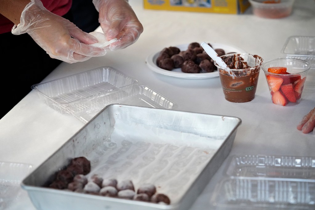 A participant flattens fresh mochi before deciding whether to add anko (sweet red-bean paste formed into a ball), Nutella or fresh strawberries during a Konko Mission of Wahiawa mochitsuki demonstration Saturday, Dec. 14, 2024, at the Japanese Cultural Center of Hawai’i in Honolulu. Or you could add all three if you dare. (Kevin Fujii/Civil Beat/2024)