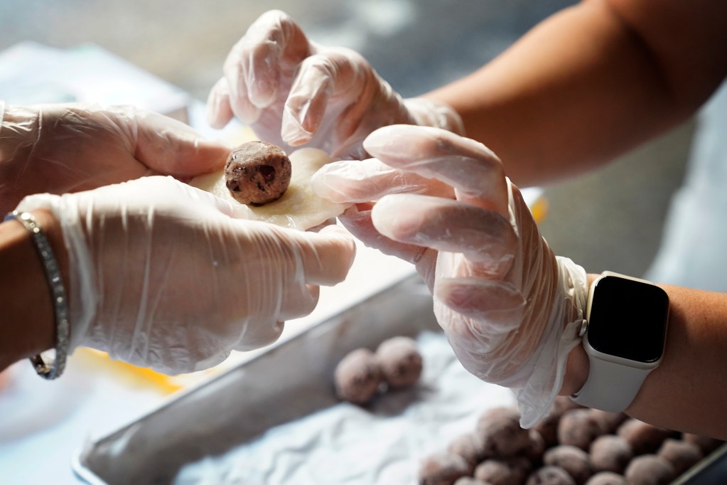 A participant learns how to fold anko (a ball of sweet red-bean paste) into fresh mochi during a Konko Mission of Wahiawa mochitsuki demonstration Saturday, Dec. 14, 2024, at the Japanese Cultural Center of Hawai’i in Honolulu. Part of the festival is to teach and learn Japanese cultural traditions. (Kevin Fujii/Civil Beat/2024)