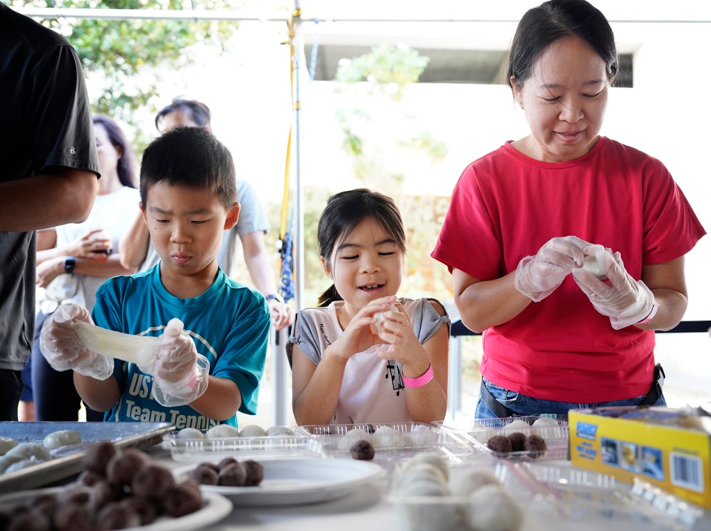 Logan, 10, from left, stretches his fresh mochi while his younger sister Lindsey, 8, and mom Debbie Lum of Kaneohe create a sweet treat during a Konko Mission of Wahiawa mochitsuki demonstration Saturday, Dec. 14, 2024, at the Japanese Cultural Center of Hawai’i in Honolulu. (Kevin Fujii/Civil Beat/2024)