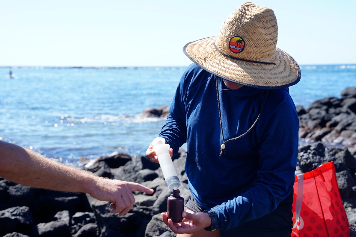 University of Hawaii Hilo Dr. Steve Colbert points out how marine-science undergraduate Sky Skiwo gathers a sample to Kohala Center volunteers Tuesday, Dec. 17, 2024, at Kahalu’u Bay in Kailua-Kona. Dye was placed in nearby cesspools earlier in the day. The data collected is to gauge the speed raw sewage reaches the coast.  (Kevin Fujii/Civil Beat/2024)
