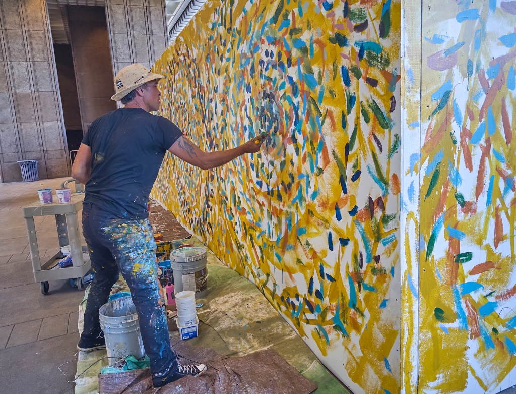 On the First Friday of February (2.7.25), Artist Solomon Enos paints lei on a construction barrier at the State Capitol assisted by members of the public who added their personal touches to the mural. (David Croxford/Civil Beat/2025)