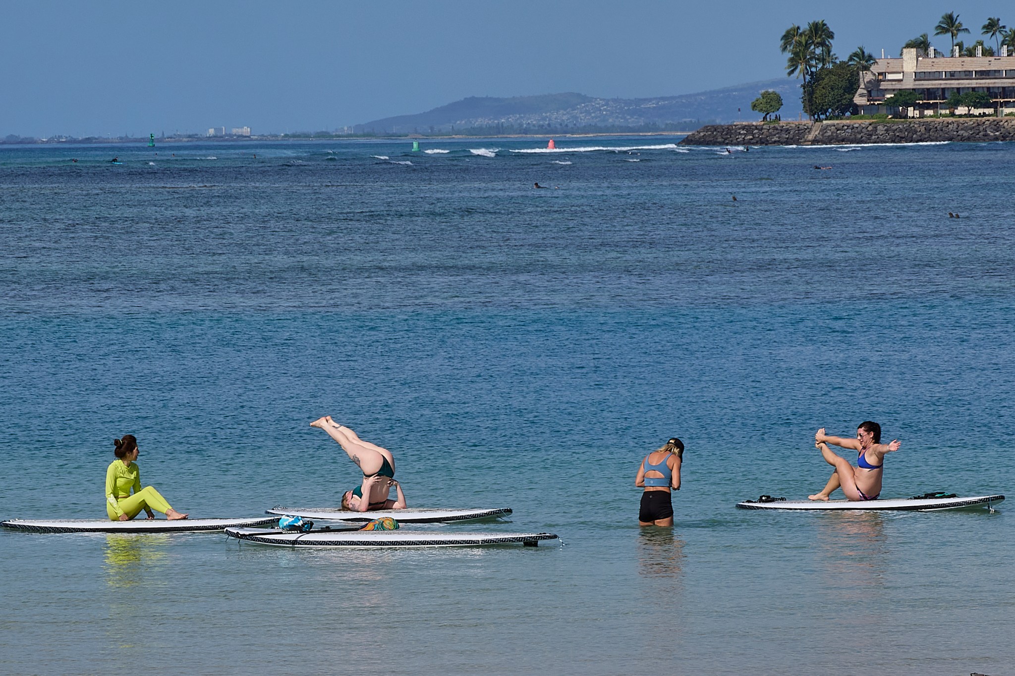 A group of ladies enjoys practice Yoga moves on Stand Up Paddle Boards in the shallow portions of the lagoon at Ala Moana Park (David Croxford/Civil Beat/2025)