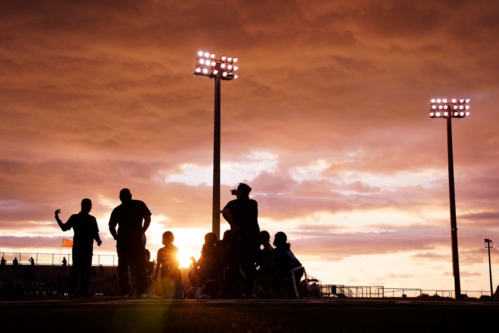 Kapolei High School players gather as the sun begins to set during halftime of the first Hawaii’i high school girls flag football game against Dreamhouse Nā Hōkū Tuesday, March 25, 2025, at Wai’anae High School in Wai’anae. (Kevin Fujii/Civil Beat/2025)