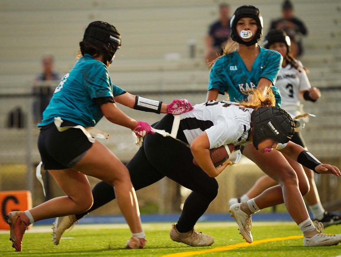 Kapolei High School’s Riah Lorenzo, left #18, de-flags Dreamhouse Nā Hōkū’s Hauoli Pualilihau, #15, as Kapolei’s Azelia Pantaleon, #14, removes Pualiliihau’s other flag during the first Hawai’i high school girls flag football game between and Kapolei is played Tuesday, March 25, 2025, at Wai’anae High School in Wai’anae. (Kevin Fujii/Civil Beat/2025)