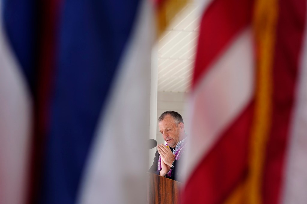 The Hawaii state and United States flags frame Gov. Josh Green as he applauds during the Daniel K. Akaka State Veterans Home dedication ceremony Wednesday, March 26, 2025, in Kapolei. (Kevin Fujii/Civil Beat/2025)