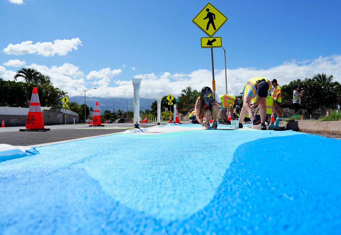 Representing the various hues of blue from salt water to fresh water, community volunteer painters Mikaela Petrilli, left, and her mom Robin Liles fill in their light-blue color at the South Maui “Quick Build” at the intersection of Kenolio Road and Alulike Street Saturday, May 3, 2025, in Kīhei. The Maui Metropolitan Planning Organization says painting a street mural will bring color and safety to this busy residential corridor. (Kevin Fujii/Civil Beat/2025)