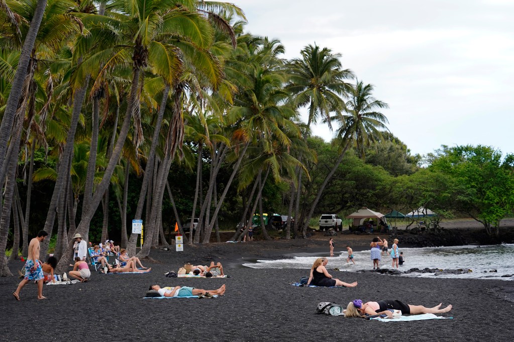 People enjoy Punaluʻu Black Sand Beach Friday, May 23, 2025, in Pāhala. Developers Black Sand Beach LLC defaulted on a $3.4 million mortgage. A district court ordered the property they planned to develop into residential, tourist and commercial into foreclosure. (Kevin Fujii/Civil Beat/2025)