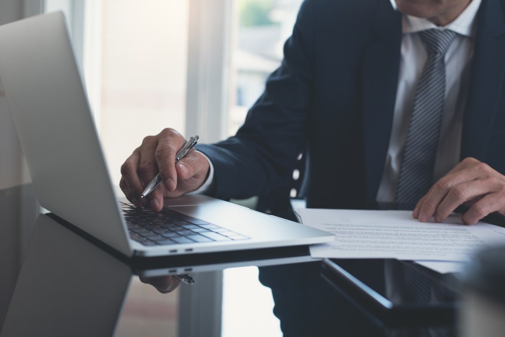Businessman working on laptop computer with paper document on table at modern office.