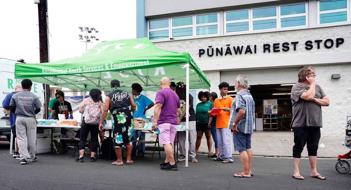 RYSE gives out pet food, toiletries, laundry detergent, meals and a drink outside of the Pūnawai Rest Stop Friday, April 25, 2025, in Honolulu. This area is known for its homeless population. RYSE helps the community regardless of age, but focuses its programs on getting young adults off the streets. (Kevin Fujii/Civil Beat/2025)