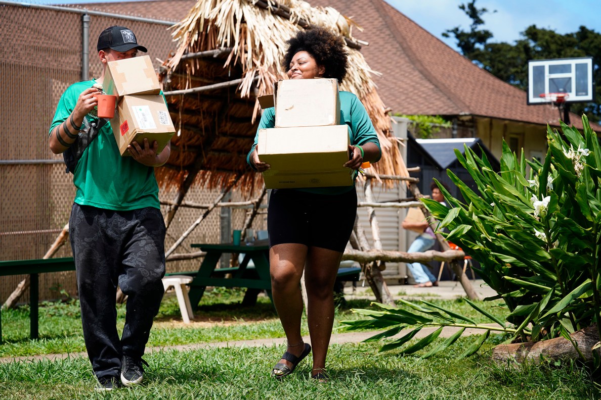 Residential Youth Services and Empowerment (RYSE) staff and residents Brody Craig, 21, from left, and Kylé-Ann Bobo, 23, carry toiletry supplies while Mason Wallace, 20, closes the storage shed Tuesday, June 3, 2025, in Kailua. They’re heading for an office to put together toiletry kits to handout when they do outreach on the streets. (Kevin Fujii/Civil Beat/2025)