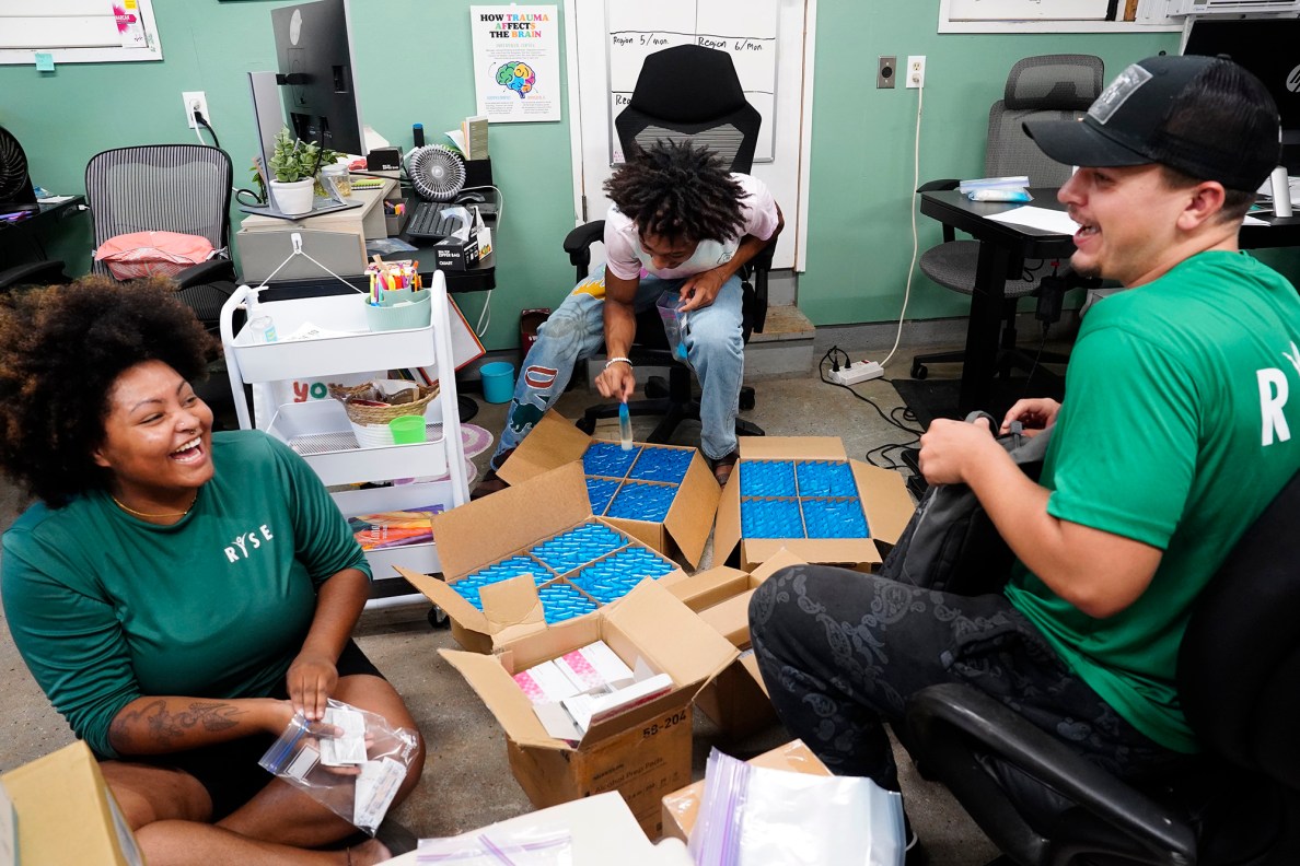 Residential Youth Services and Empowerment (RYSE) staff and residents Kylé-Ann Bobo, 23, from left, Mason Wallace, 20, and Brody Craig, 21, enjoy a light moment Tuesday, June 3, 2025, in Kailua. They’re in an office putting together toiletry kits to handout when they do outreach on the streets. (Kevin Fujii/Civil Beat/2025)